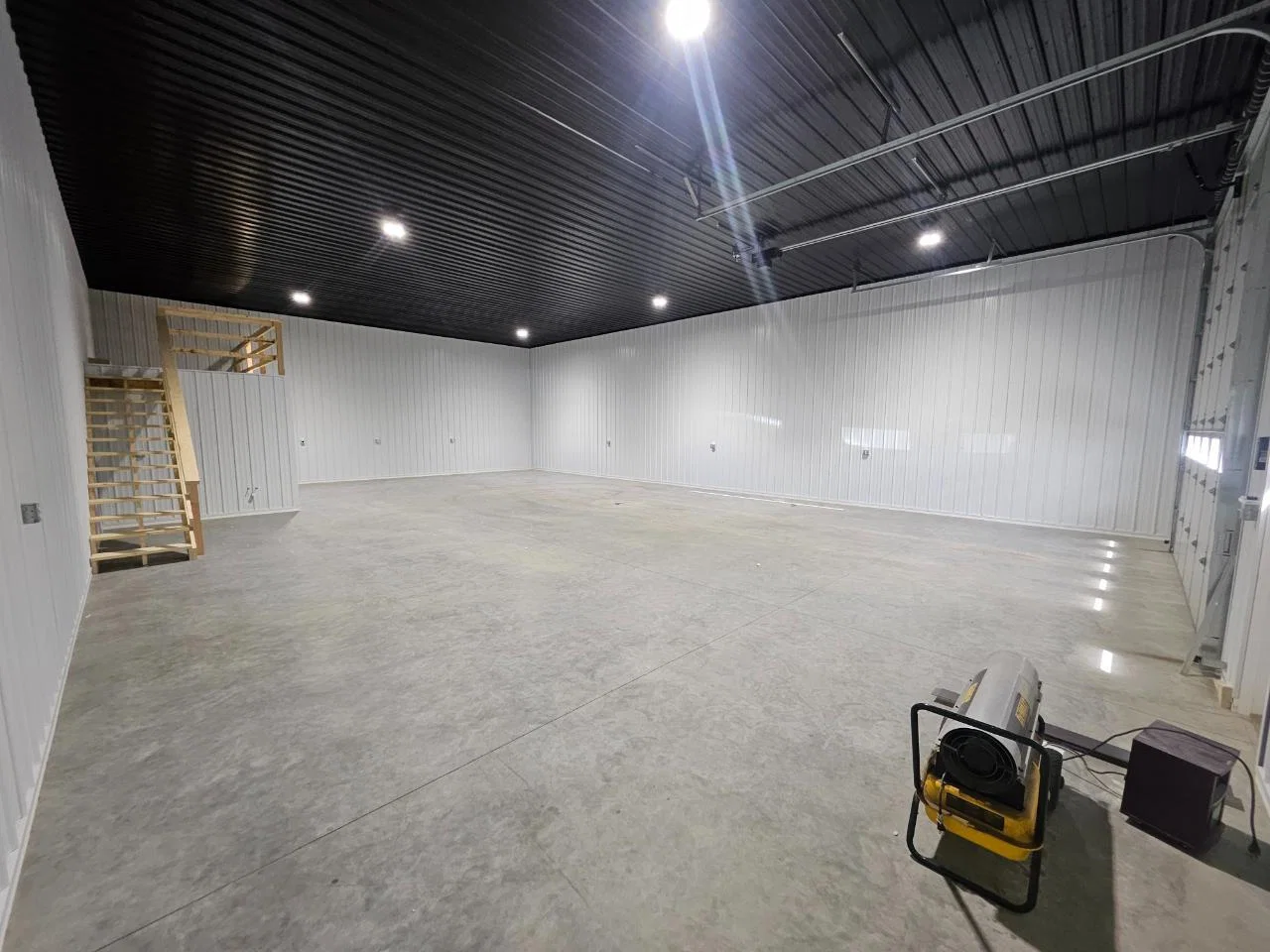Heated shop condo interior with black steel ceiling, LED lighting, and a clean concrete slab